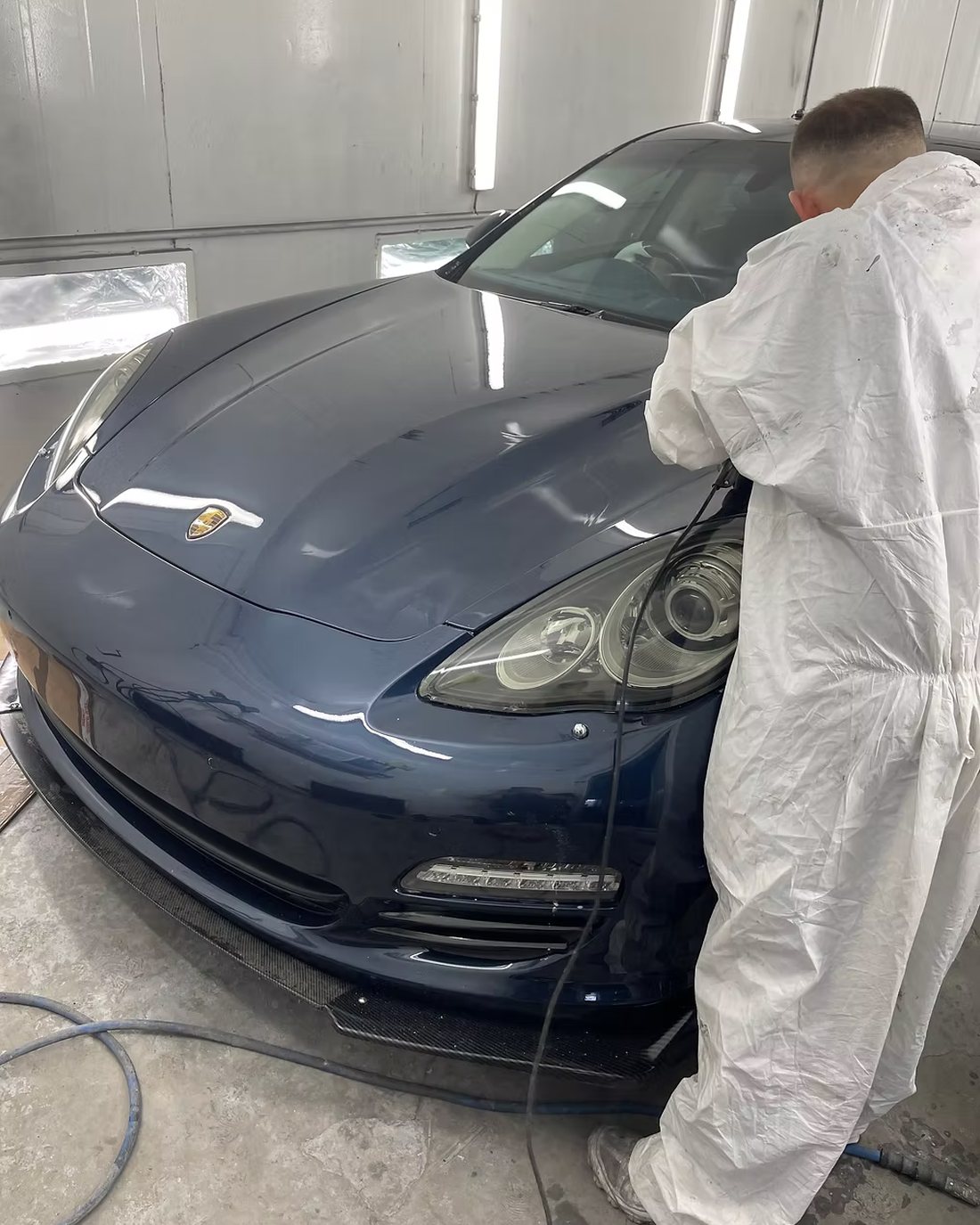 A technician in a paint suit working on a dark blue Porsche Panamera inside the N17 Bodyworks spray booth